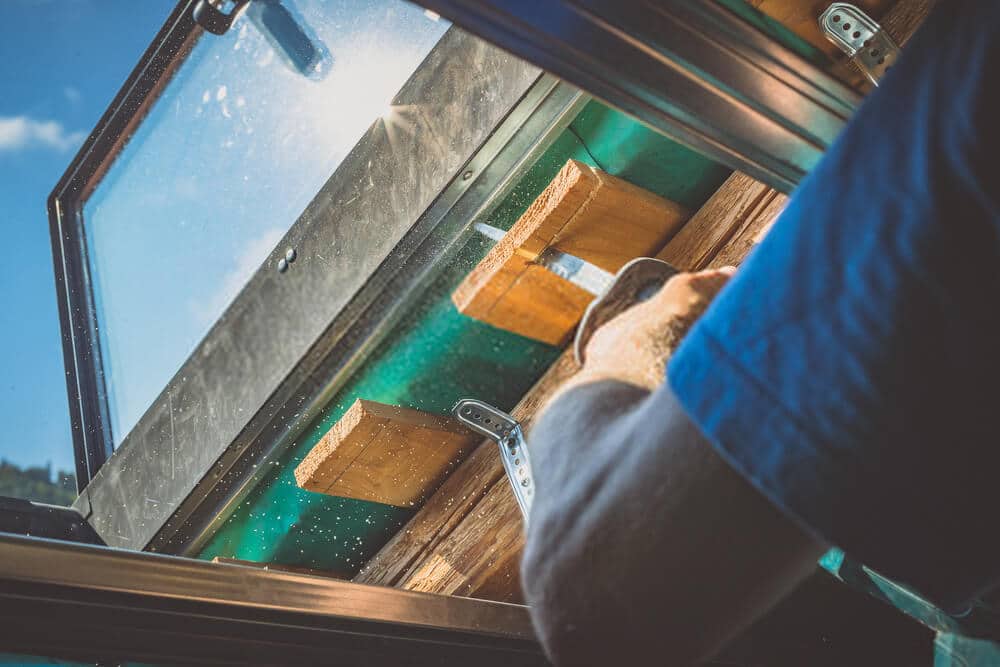 cutting-a-board-of-wood A person is cutting a board of wood next to a window with a reciprocating saw